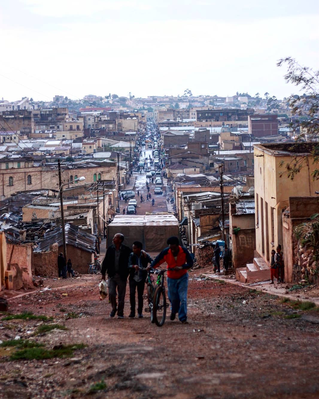 Residents walking up an unpaved street surrounded by closely built homes in Abashawl
